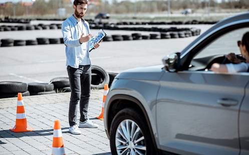 Ein Mann steht auf einem Trainingsgelände vor einem Auto und gibt Anweisungen.