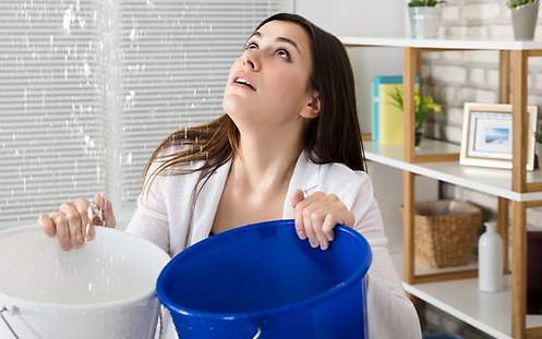 Eine Frau fängt mit Eimern die Folgen eines Wasserschadens auf