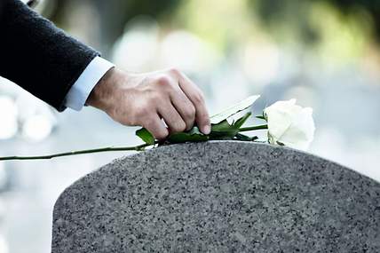 Eine Person legt eine weiße Rose auf einen Grabstein nieder.