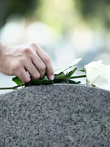 Eine Person legt eine weiße Rose auf einen Grabstein nieder.